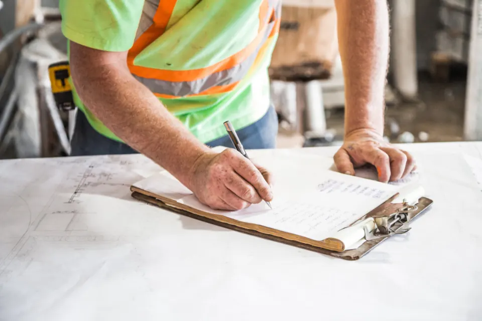 Worker in a high-visibility vest completing paperwork on a clipboard