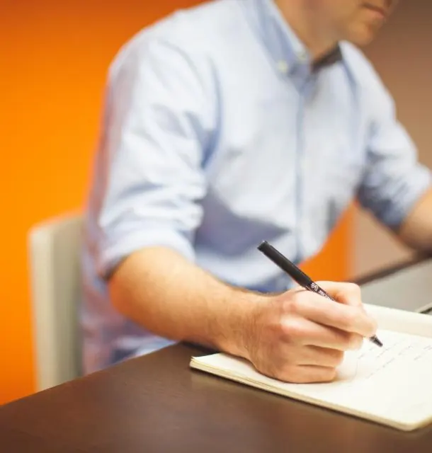 Person noting down payroll changes in a notebook next to a laptop