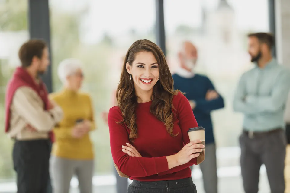 Smiling professional standing in a bright office with her colleagues talking behind her