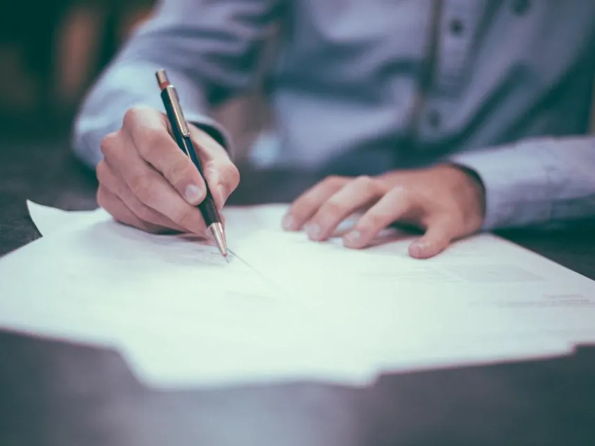 Person signing a written document at a desk