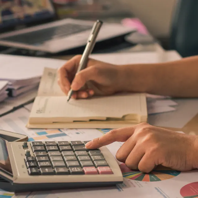 Hands checking figures on a calculator while recording entries in a ledger
