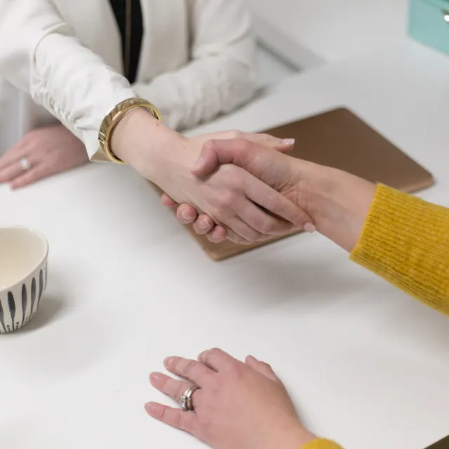Two people shaking hands across a desk after agreeing terms